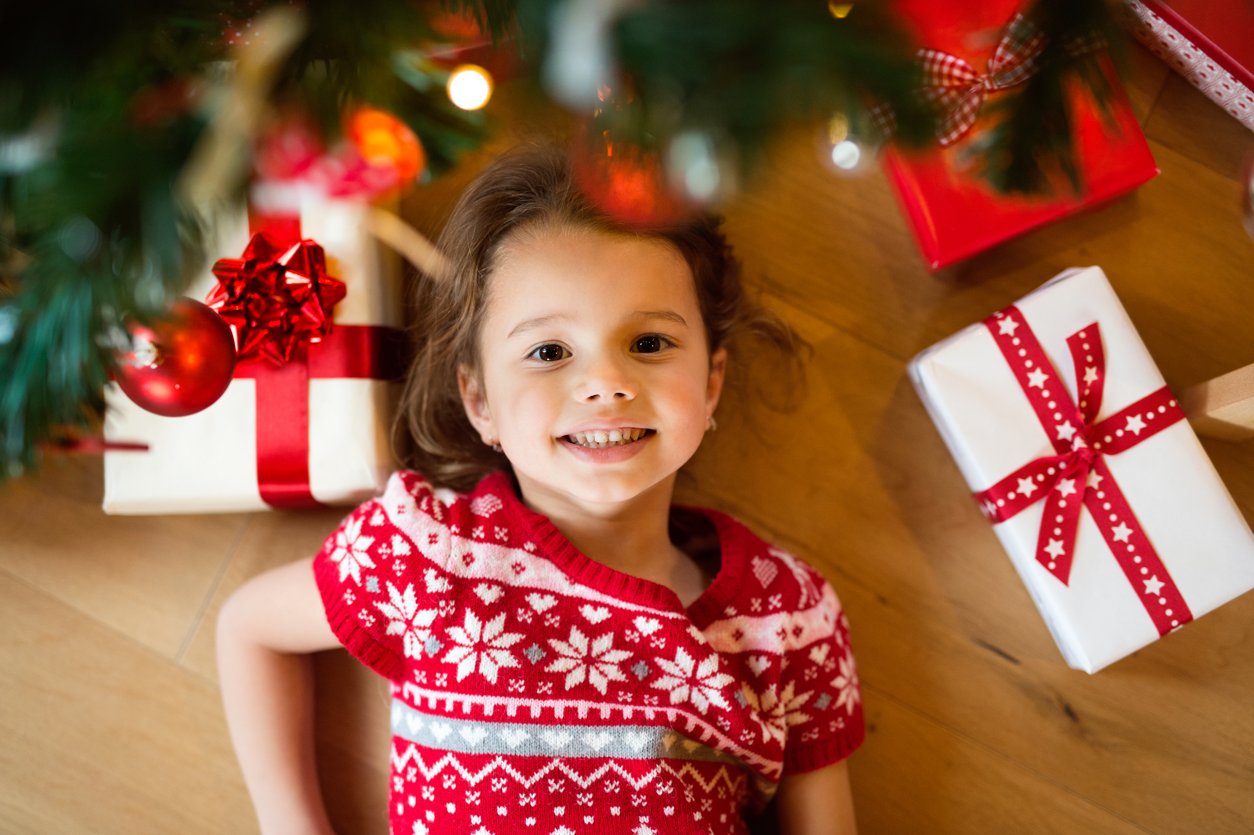 Little girl lying under Christmas tree among presents,